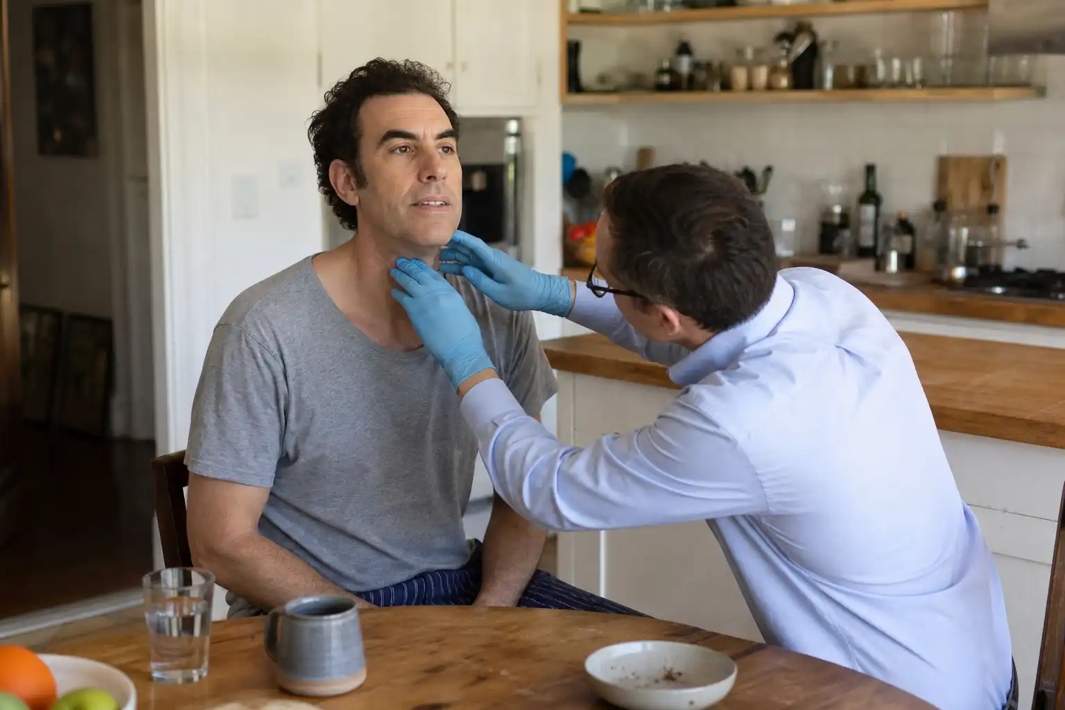 Quelqu'un examine un objet, autour de sacha baron cohen, dans une cuisine.